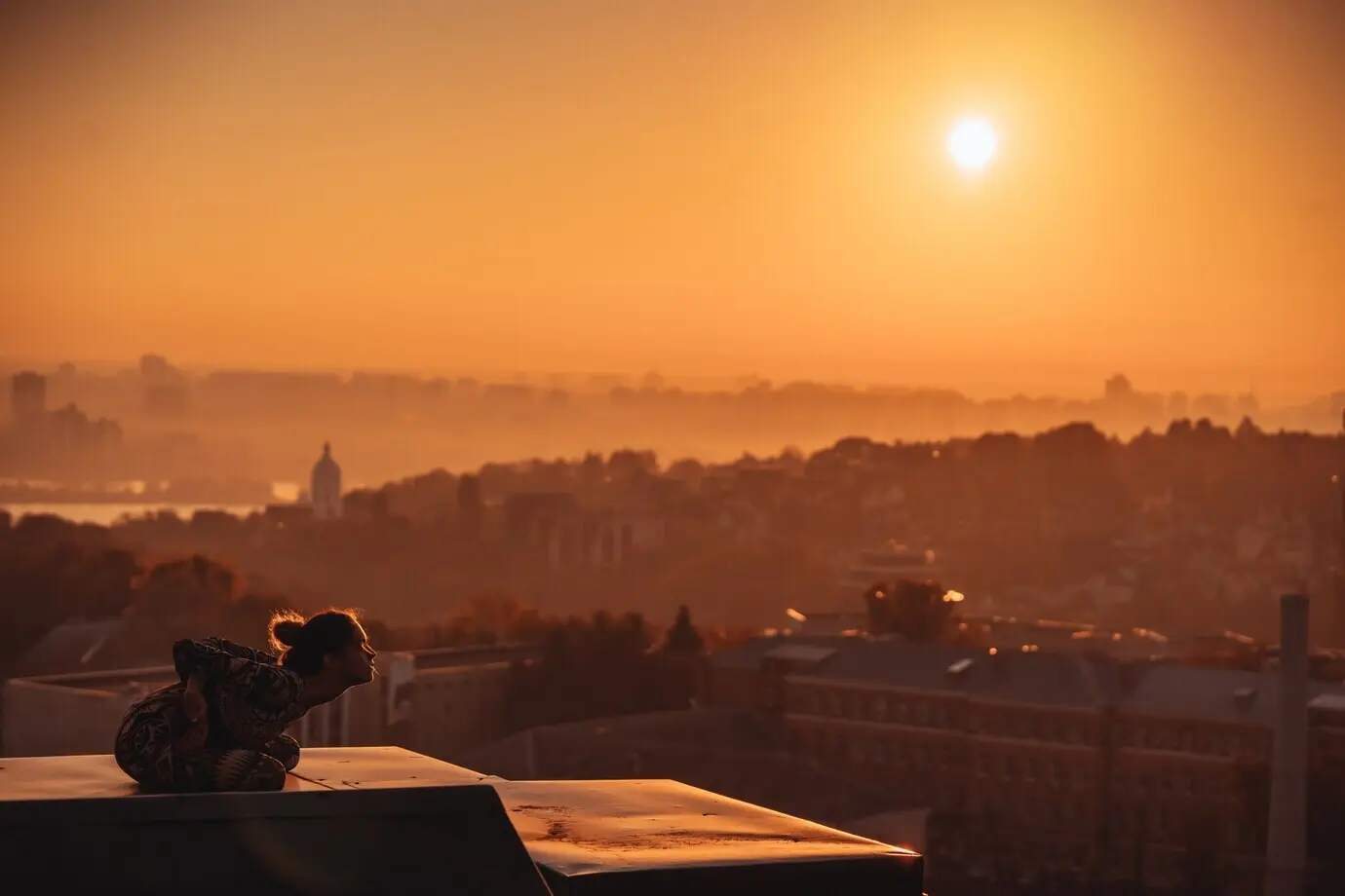 A woman practicing yoga on a skyscraper rooftop in a big city.