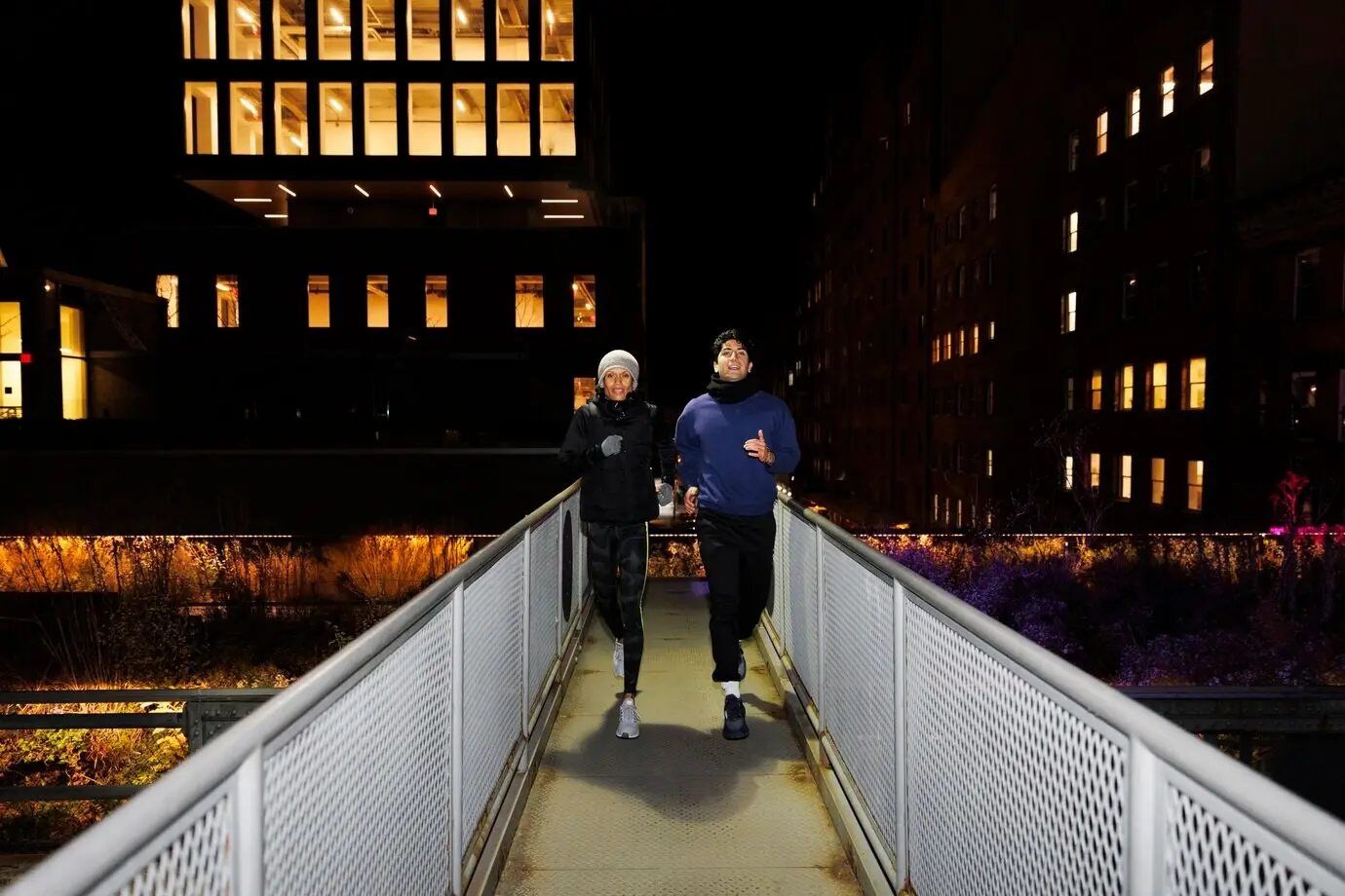 Friends running on a city bridge at night.